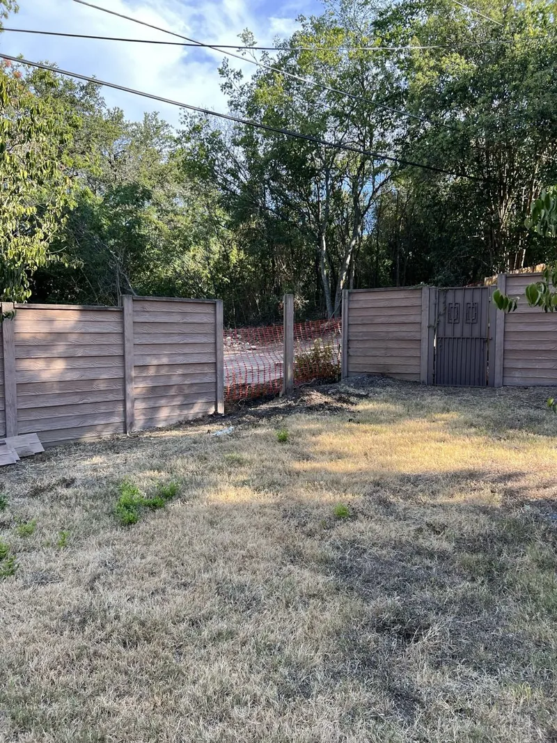 The side yard before: dry dead grass, a bare fence and orange safety netting