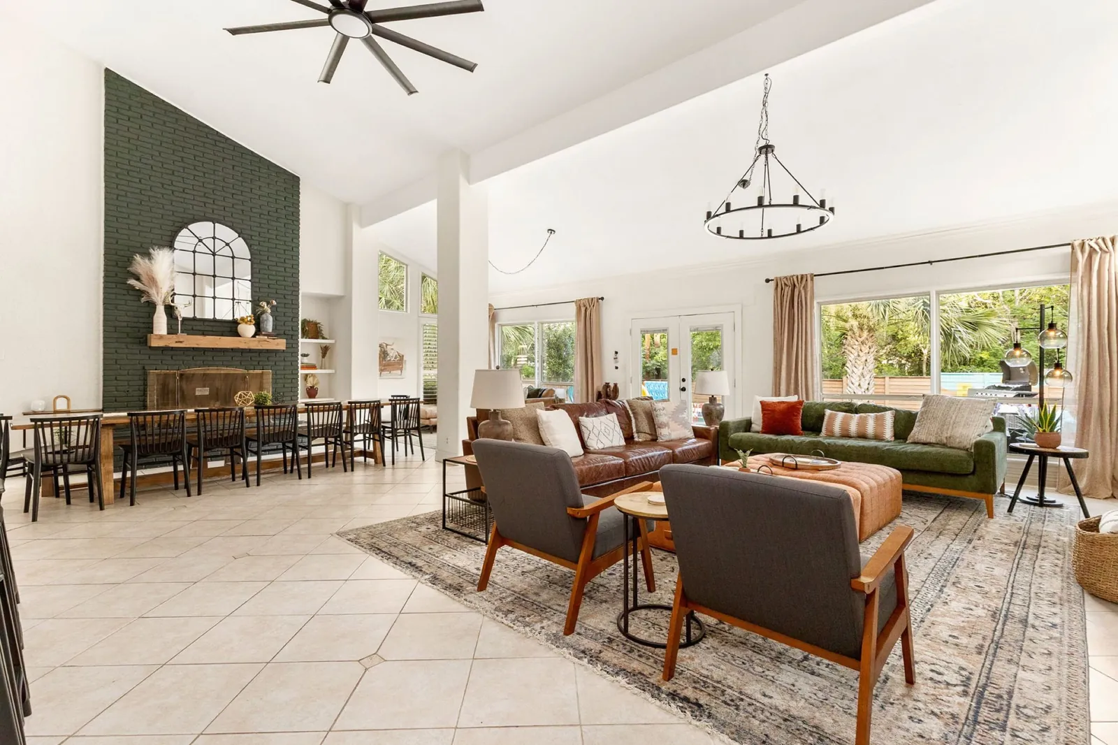 The great room at Climbing Rose: a green brick fireplace, a long farm table, leather sofas and an orange ottoman under a black chandelier