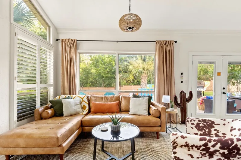 Sunroom after: a tan leather sectional, a cowhide chair and a wicker pendant