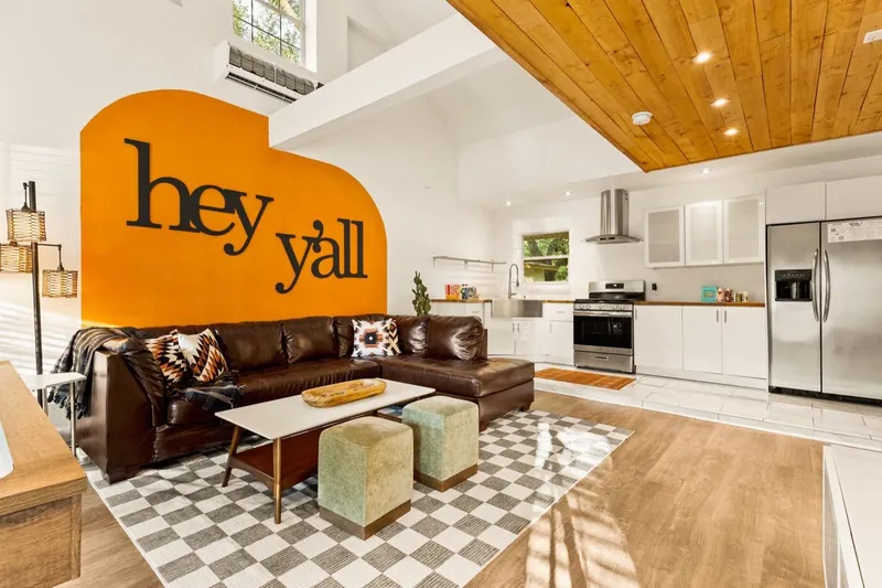 Game room in 2025: hey y’all on an orange arch, a checkerboard rug and green ottomans