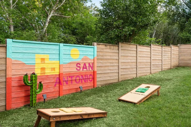 The side yard after: a bright San Antonio mural on the fence, green grass and cornhole boards