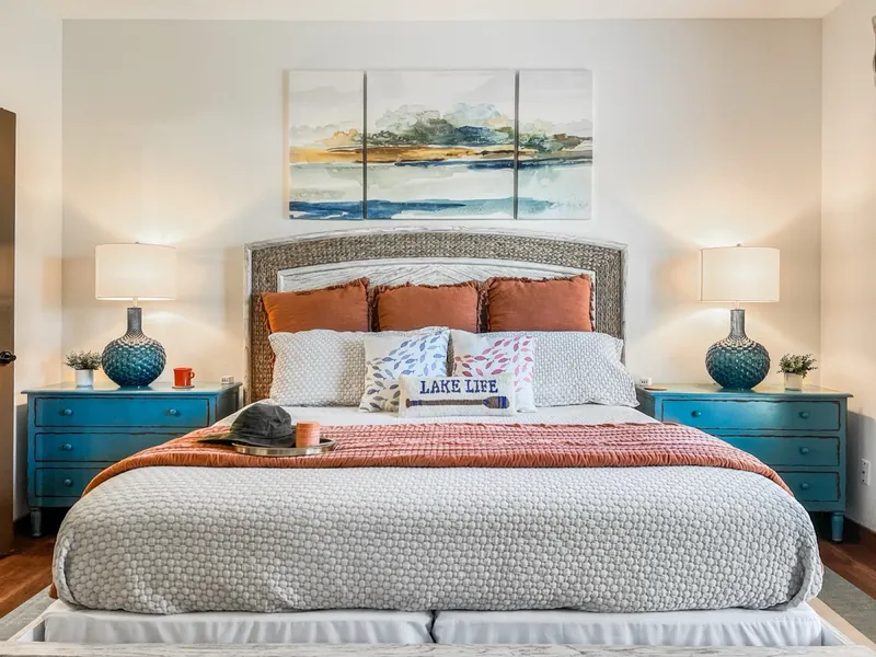 Primary suite after: lake art, teal nightstands and rust pillows