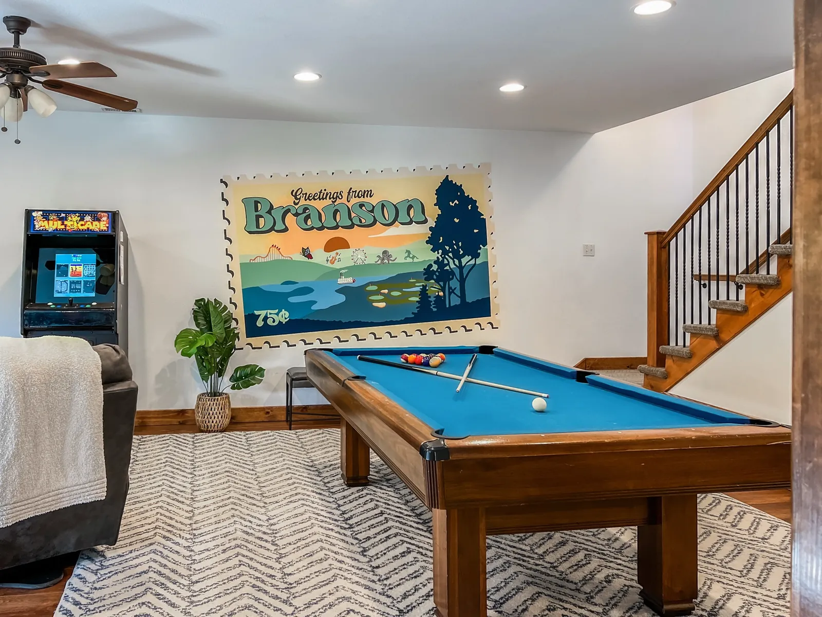 The Deep Forest Retreat game room: a blue-felt pool table, arcade cabinet and a Greetings from Branson mural